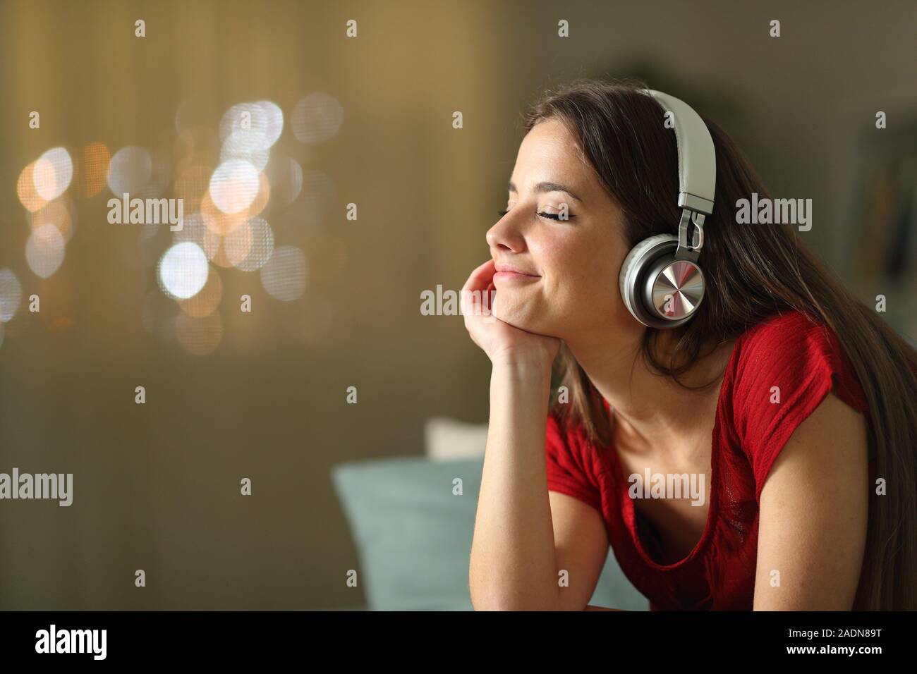 Relaxed woman listening to music wearing wireless headphones in the night sitting on a couch in the living room at home Stock Photo