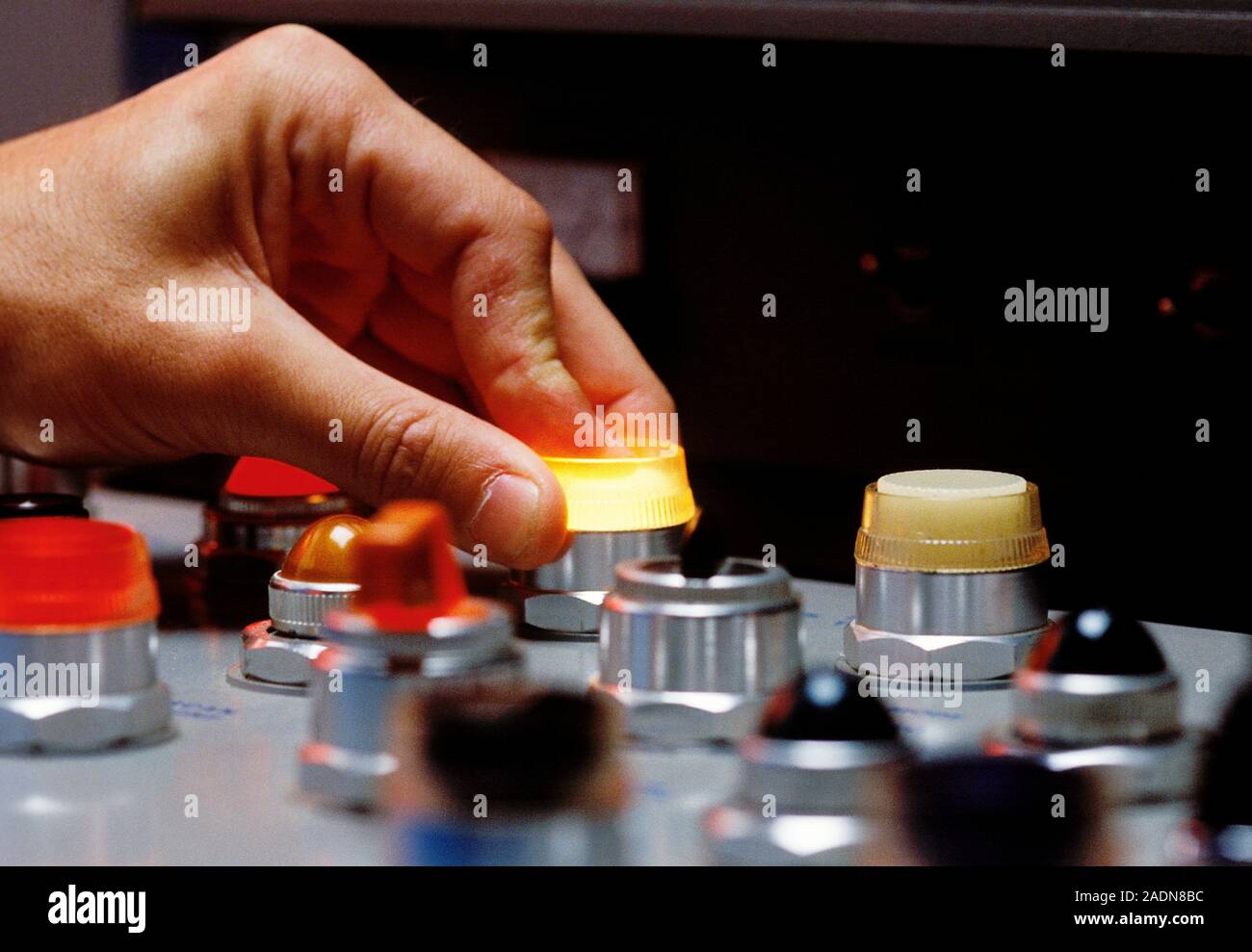 Control panel. Hand pressing a lit button on an industrial control panel. Stock Photo