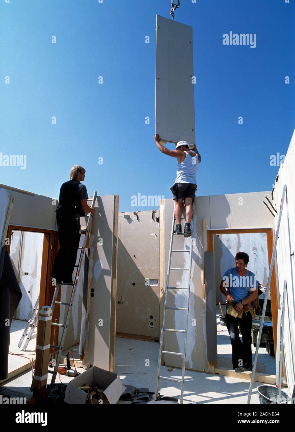 Prefabricated house construction. Worker guiding a crane-held section ...