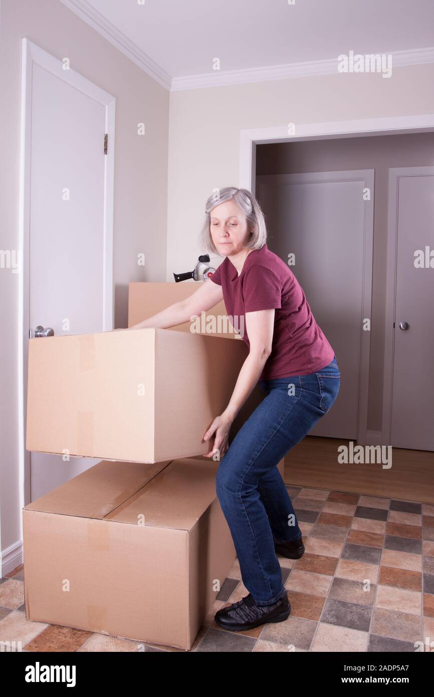 Mature grey haired woman prepares to move to another house stacks big brown boxes Stock Photo