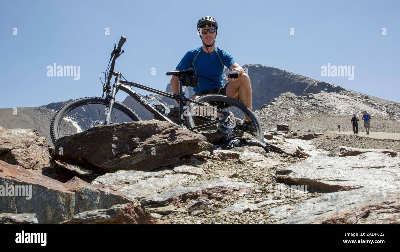 Male cyclist sitting with a mountain bike at Mirador del Corral del Veleta just below the summit of Veleta, in Sierra Nevada mountains, Granada, Spain Stock Photo