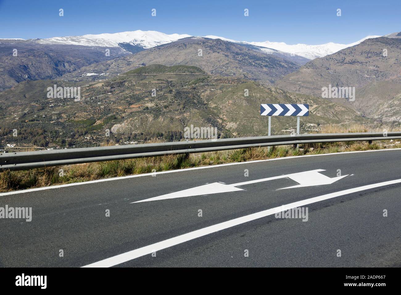 Directional arrows on the scenic A-348 road through the Alpujarra Valley between Órgiva and Torvizcón, Andalusia, Spain. Behind are the winter snow ca Stock Photo