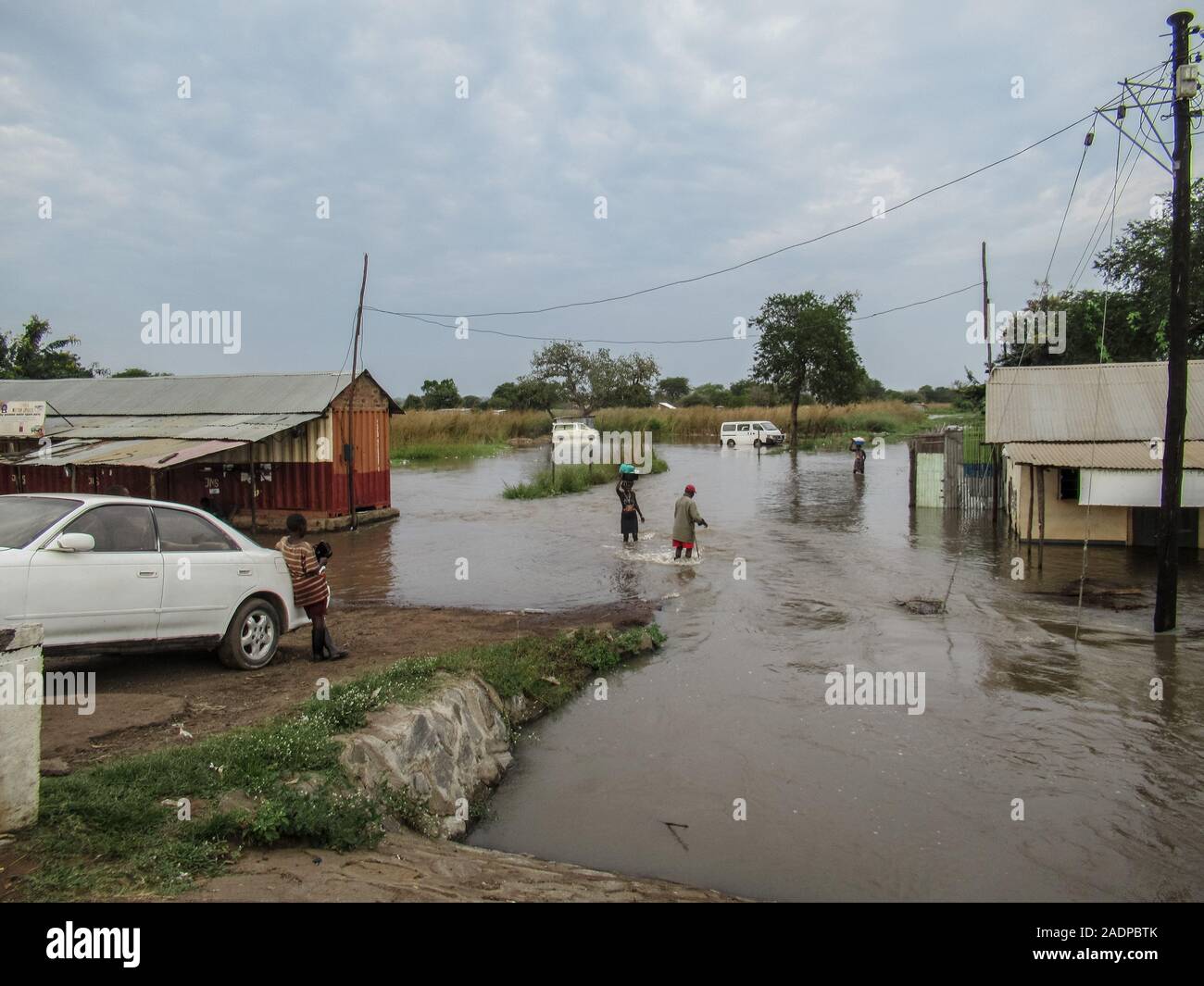 A woman carrying her belongings from a flooded home.Businesses and homes damaged by flooding in Elegu, northern Uganda, on the border with South Sudan. Thousands of people across East Africa are currently affected by flooding. Stock Photo