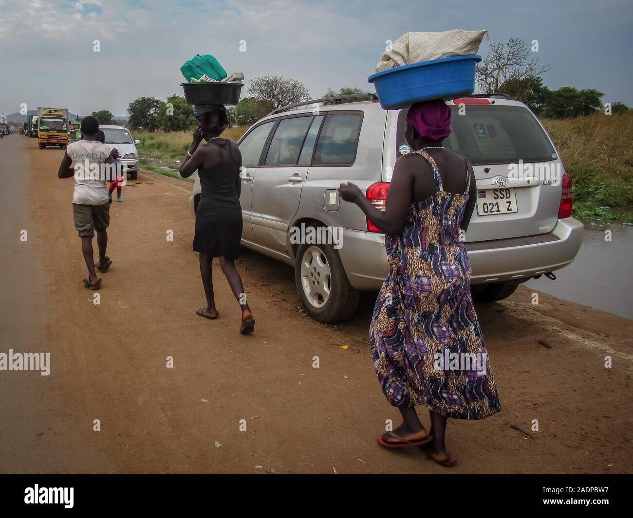 Women carrying their belongings from flooded home.Businesses and homes damaged by flooding in Elegu, northern Uganda, on the border with South Sudan. Thousands of people across East Africa are currently affected by flooding. Stock Photo