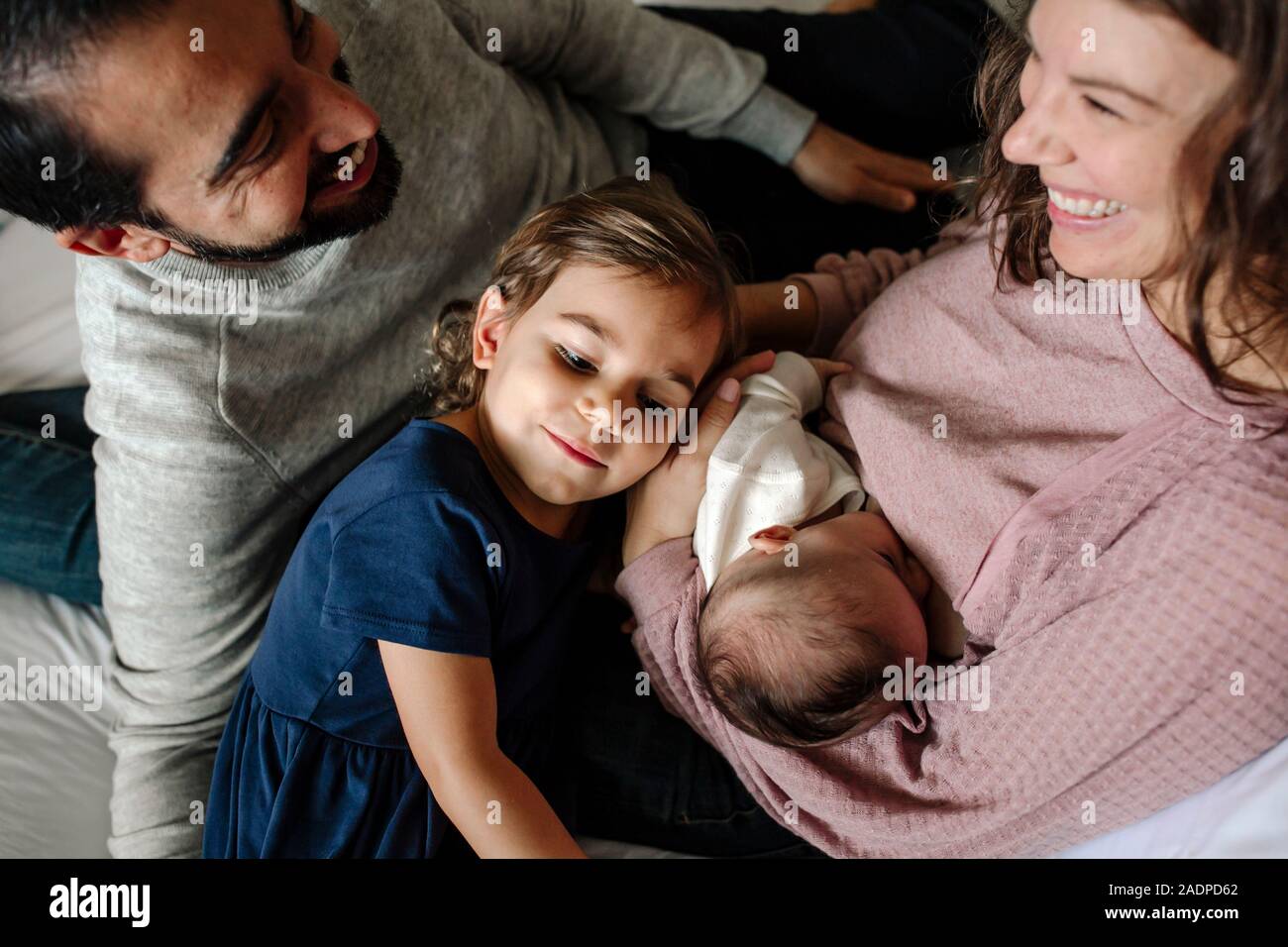 Smiling dad, mom and 4 yr old cuddle nursing newborn baby Stock Photo