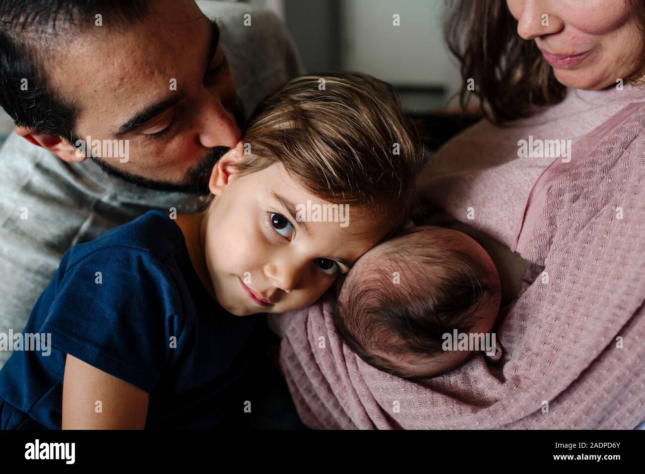 Big sister gently rests head on newborn sister as dad kisses her Stock Photo