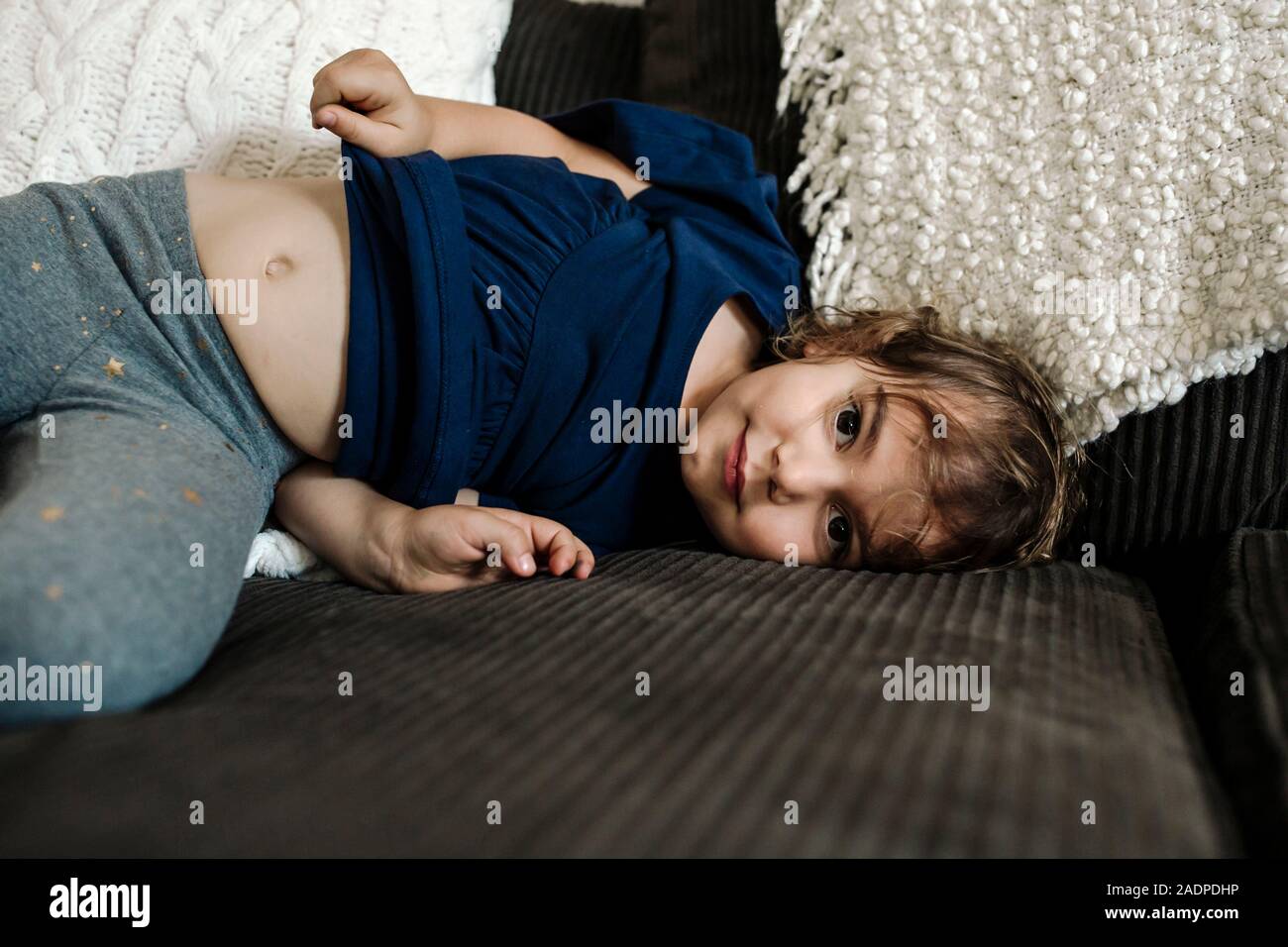 4 yr old girl lying on couch with belly showing Stock Photo