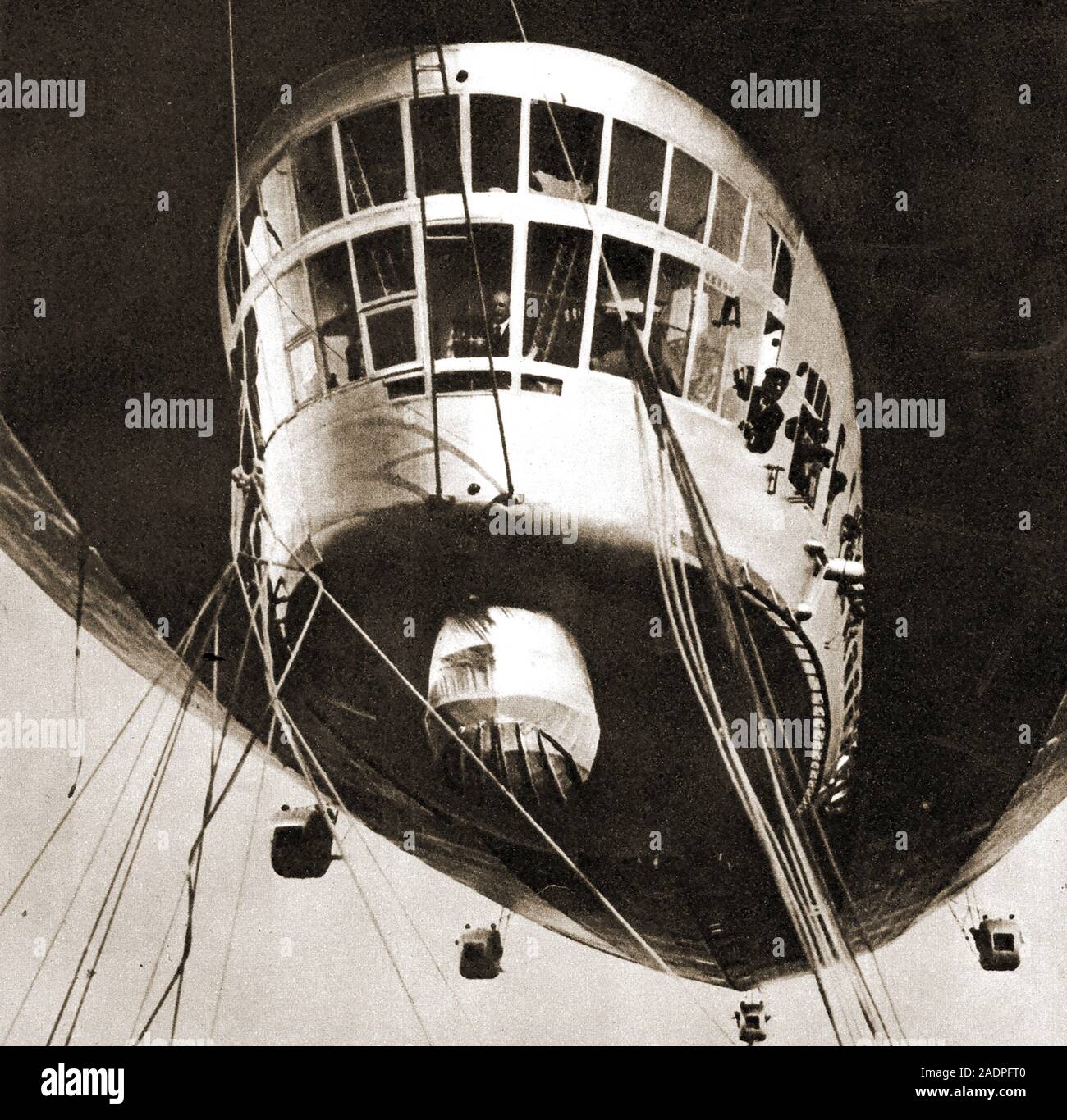 An historic photograph of the graph zeppelin showing the pilot at  the controls and passengers and crew looking out of the windows. It was propelled  by five Maybach engines. 772 feet long, 100ft wide, 107 tons displacement. It flew around the world in 1929. Stock Photo