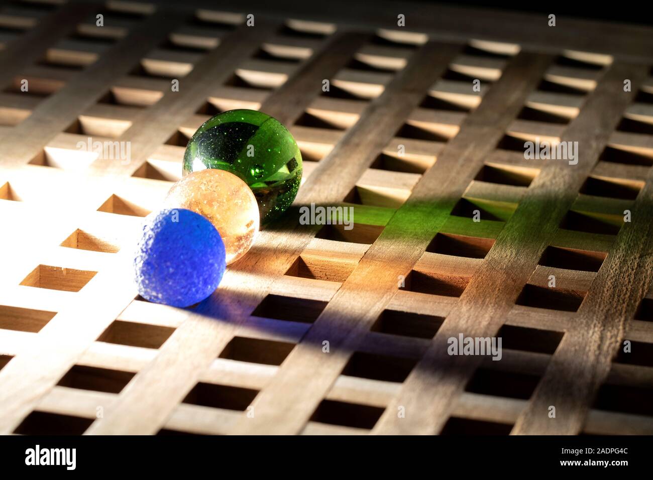 A portrait of three colorful marbles lit by a single light making them cast colorful shadows and reflections onto a wooden surface. Stock Photo