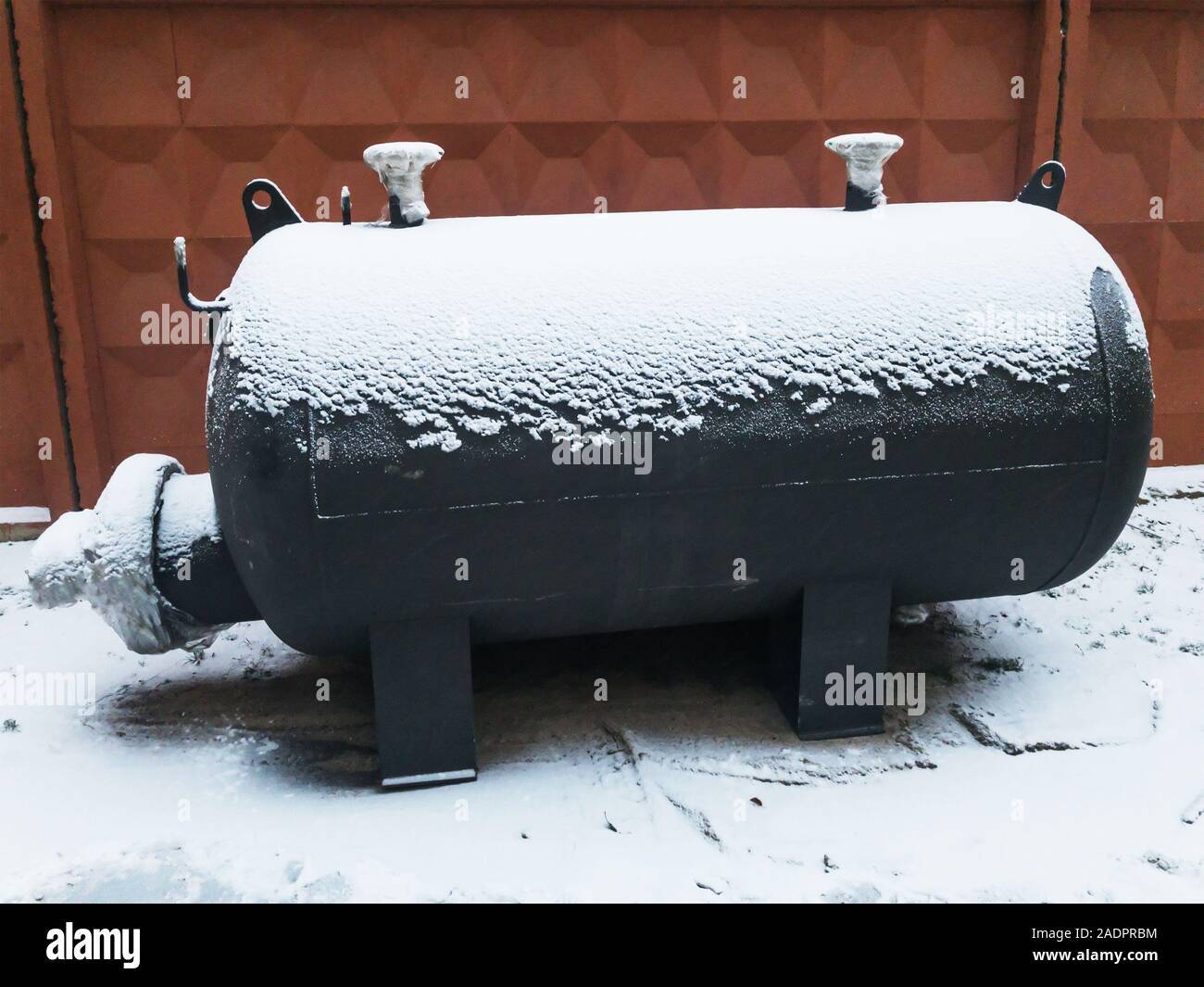 Black Industrial capacitive heater at winter under snow near brown concrete fence. Heat exchanger. Stock Photo