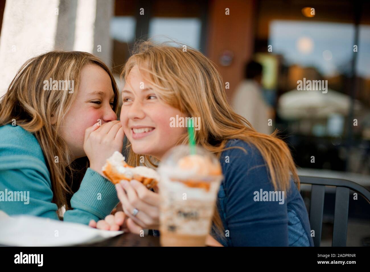 Two teenage girls whispering to each other and smiling Stock Photo - Alamy