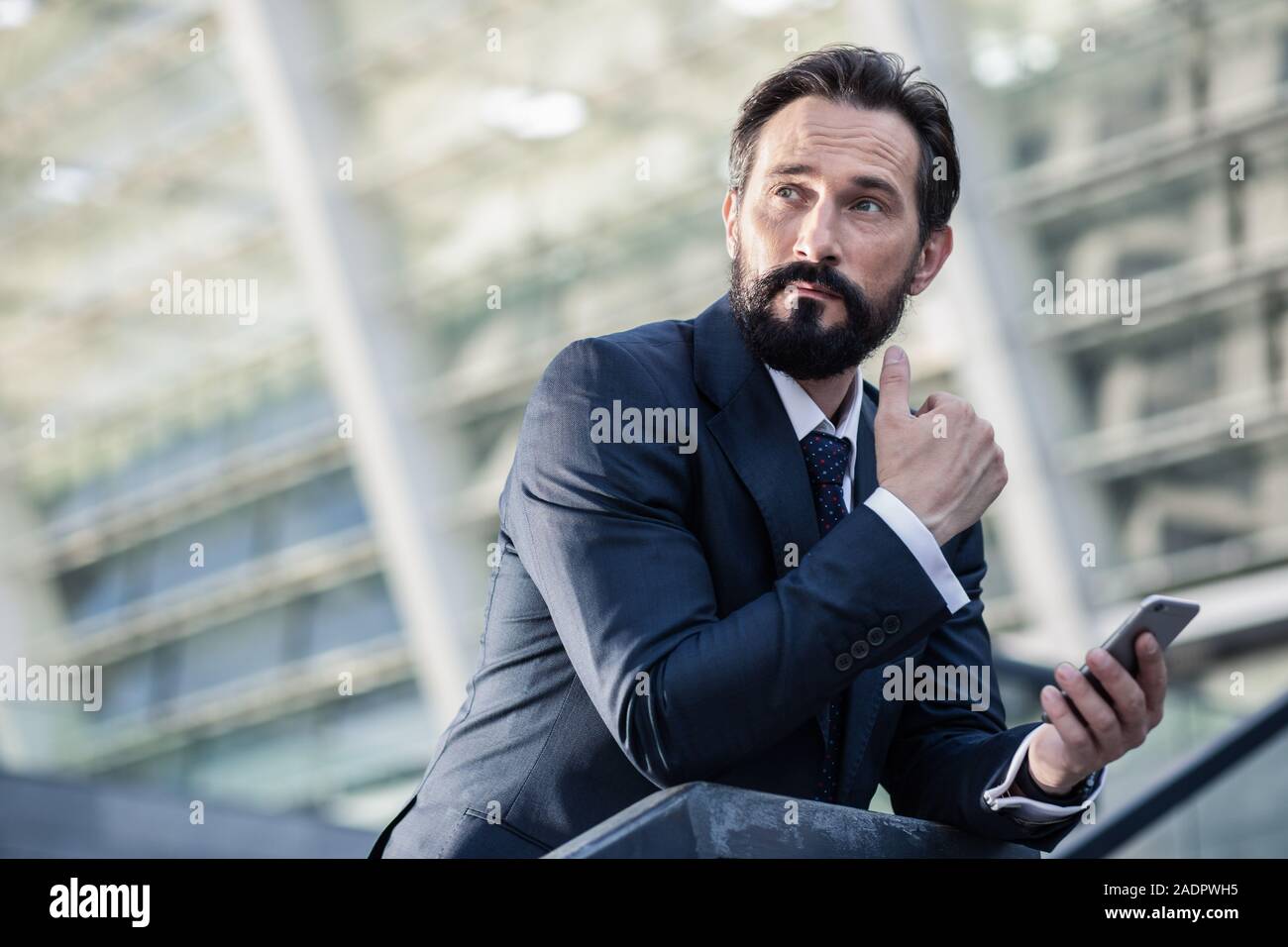 Thoughtful bearded businessman using his smartphone outdoors Stock Photo