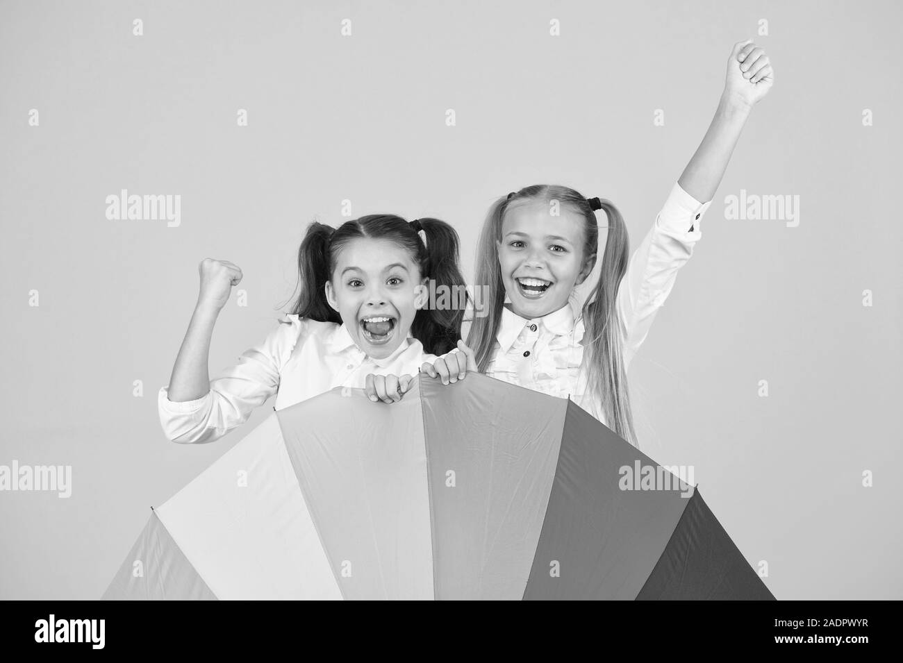 The coolest accessory in school. Happy little girls celebrating autumn holidays behind fashion accessory. Small children smiling with colorful umbrella rain accessory. Best accessory trend for fall. Stock Photo