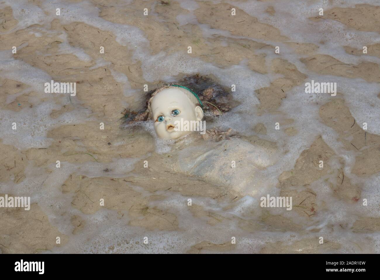 Lost doll on beach drowning in upcoming tide Stock Photo