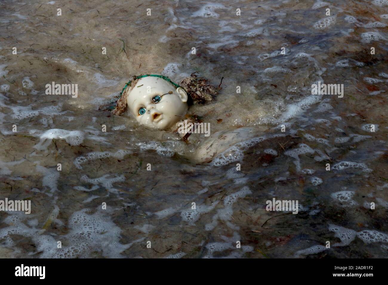 Discarded doll swallowed by polluted ocean Stock Photo