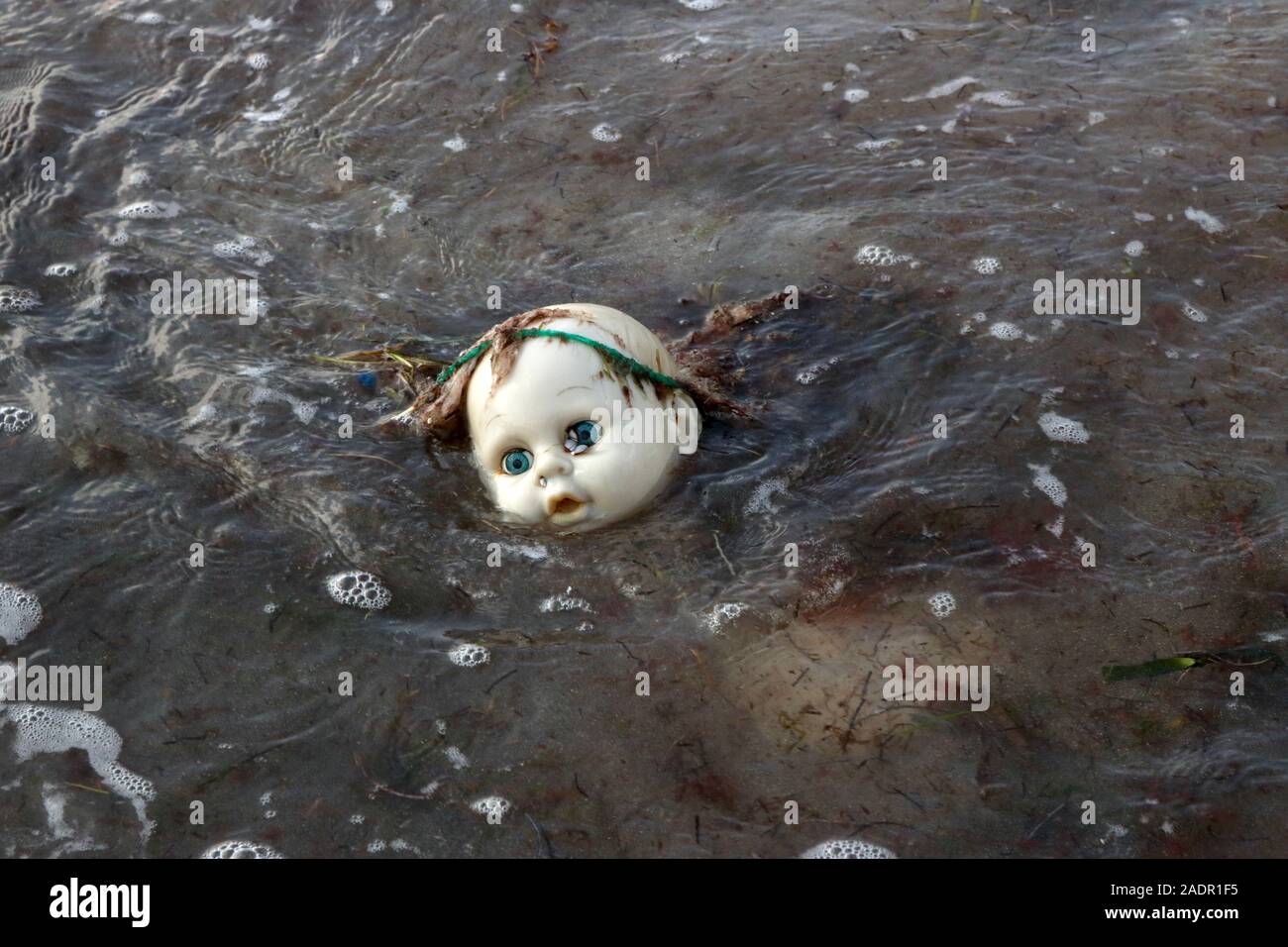 Washed up doll drowning in polluted ocean Stock Photo