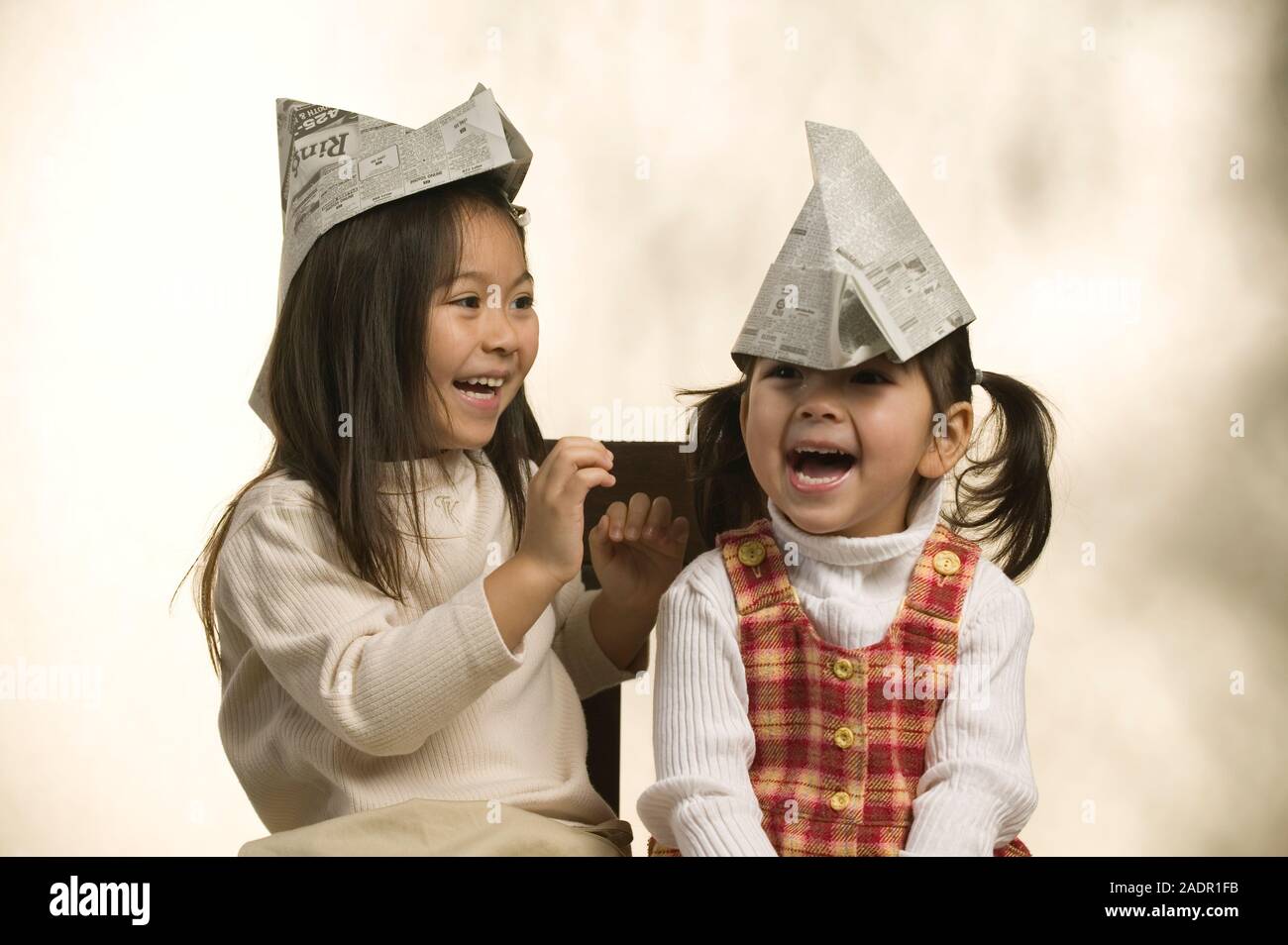 Portrait of two young Asian sisters wearing paper hats on a plain background Stock Photo