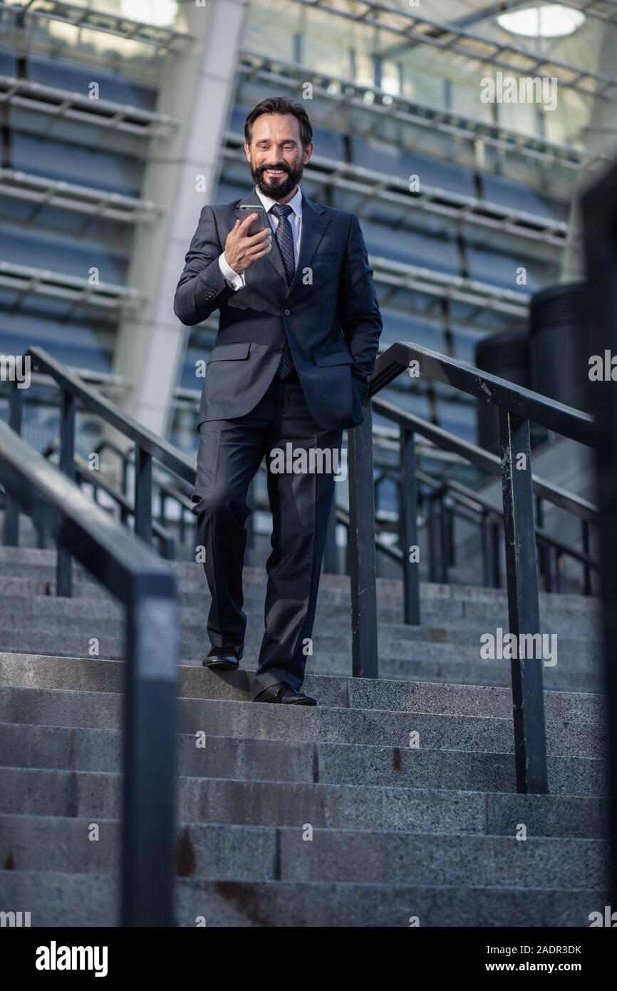 Positive bearded businessman walking down the stairs Stock Photo