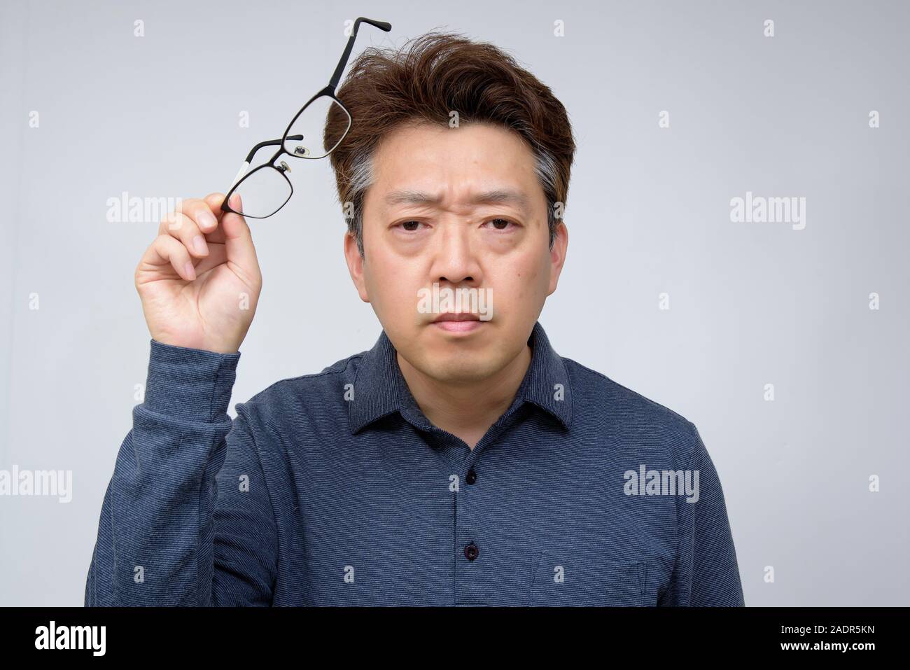 Asian middle-aged male trying to take off glasses and see something. poor sight, presbyopia, myopia. Stock Photo