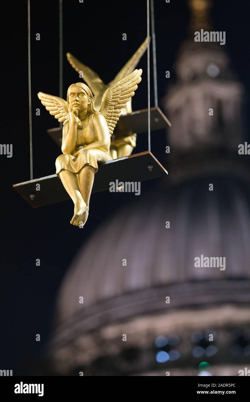 Lunch Break - 35 gilded angels sitting on randomly arranged bars, suspended from St Paul's Plinth, outside St Paul's underground tube station Stock Photo