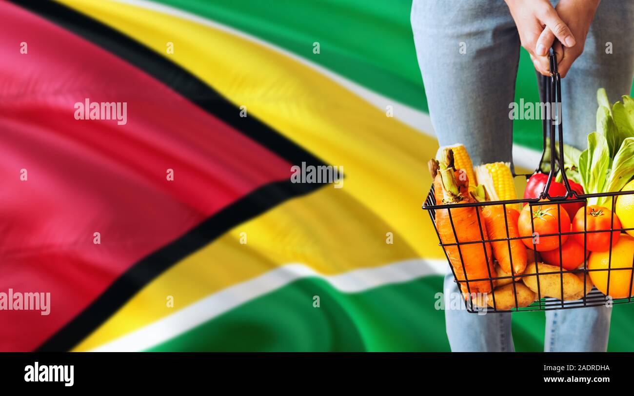 Woman is holding supermarket basket, Guyana waving flag background. Economy concept for fresh fruits and vegetables. Stock Photo