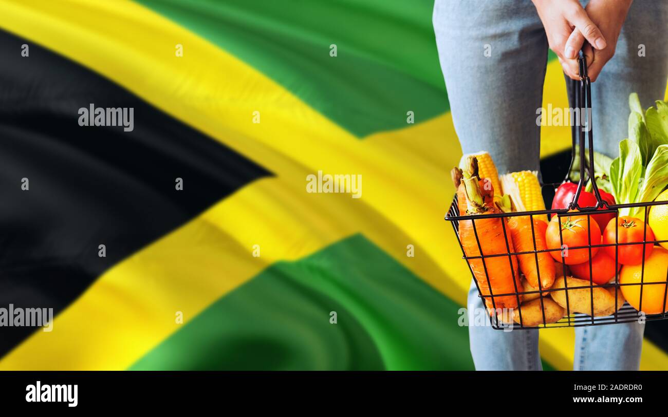 Woman is holding supermarket basket, Jamaica waving flag background
