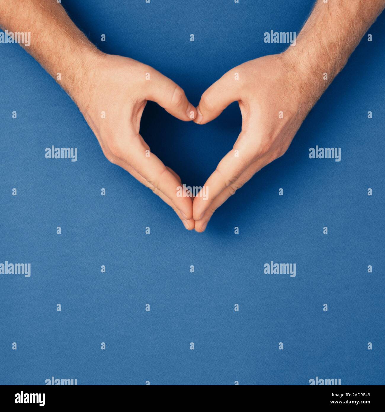 Male hands in shape of heart on classic blue background. Healthcare and chirty, color of year concept. Stock Photo