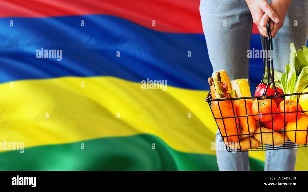 Woman is holding supermarket basket, Mauritius waving flag background. Economy concept for fresh fruits and vegetables. Stock Photo