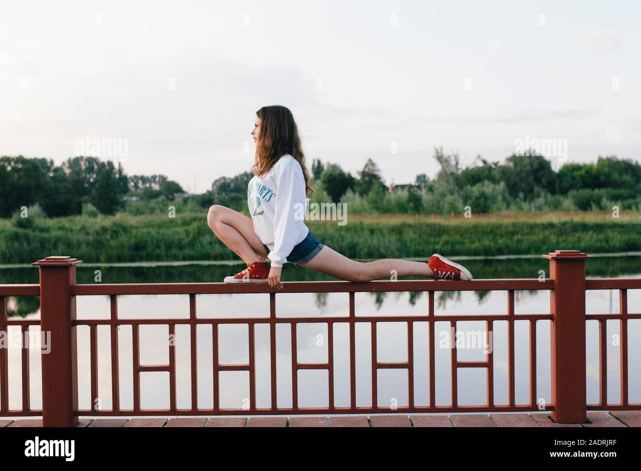 woman stretches her legs on a fence by the river Stock Photo