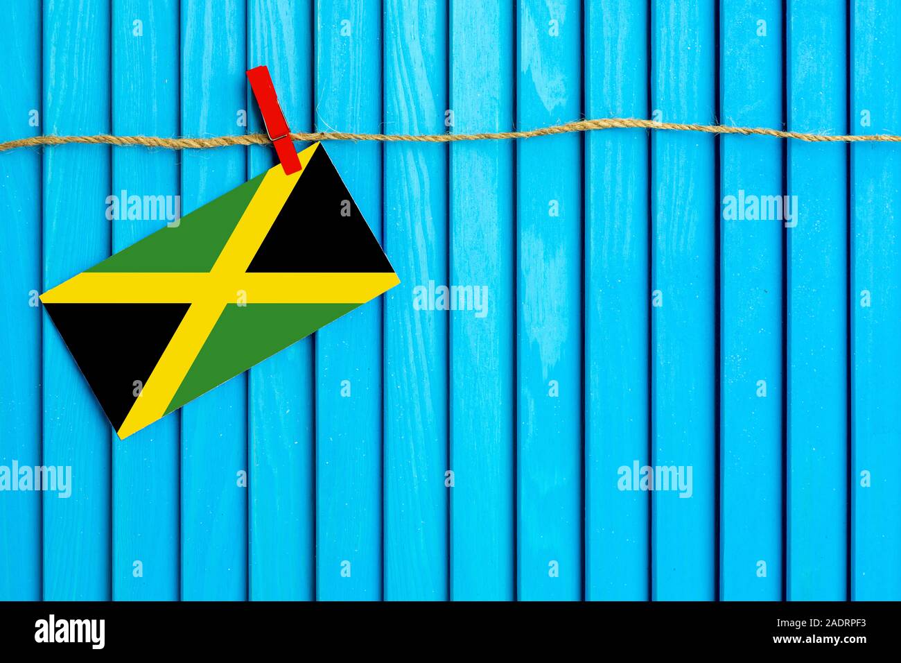 Flag of Jamaica hanging on clothesline attached with wooden clothespins on aqua blue wooden background. National day concept. Stock Photo