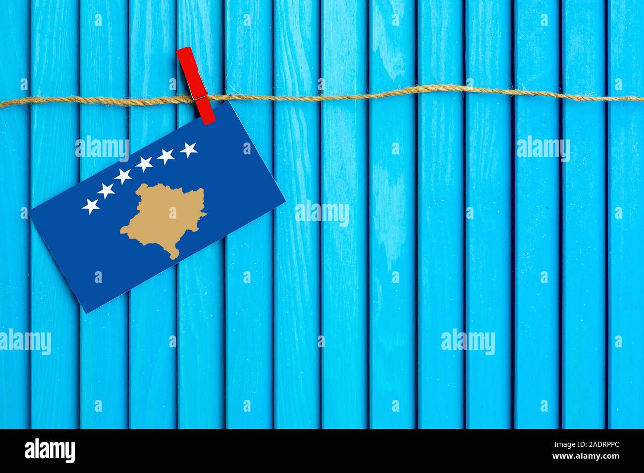Flag of Kosovo hanging on clothesline attached with wooden clothespins on aqua blue wooden background. National day concept. Stock Photo