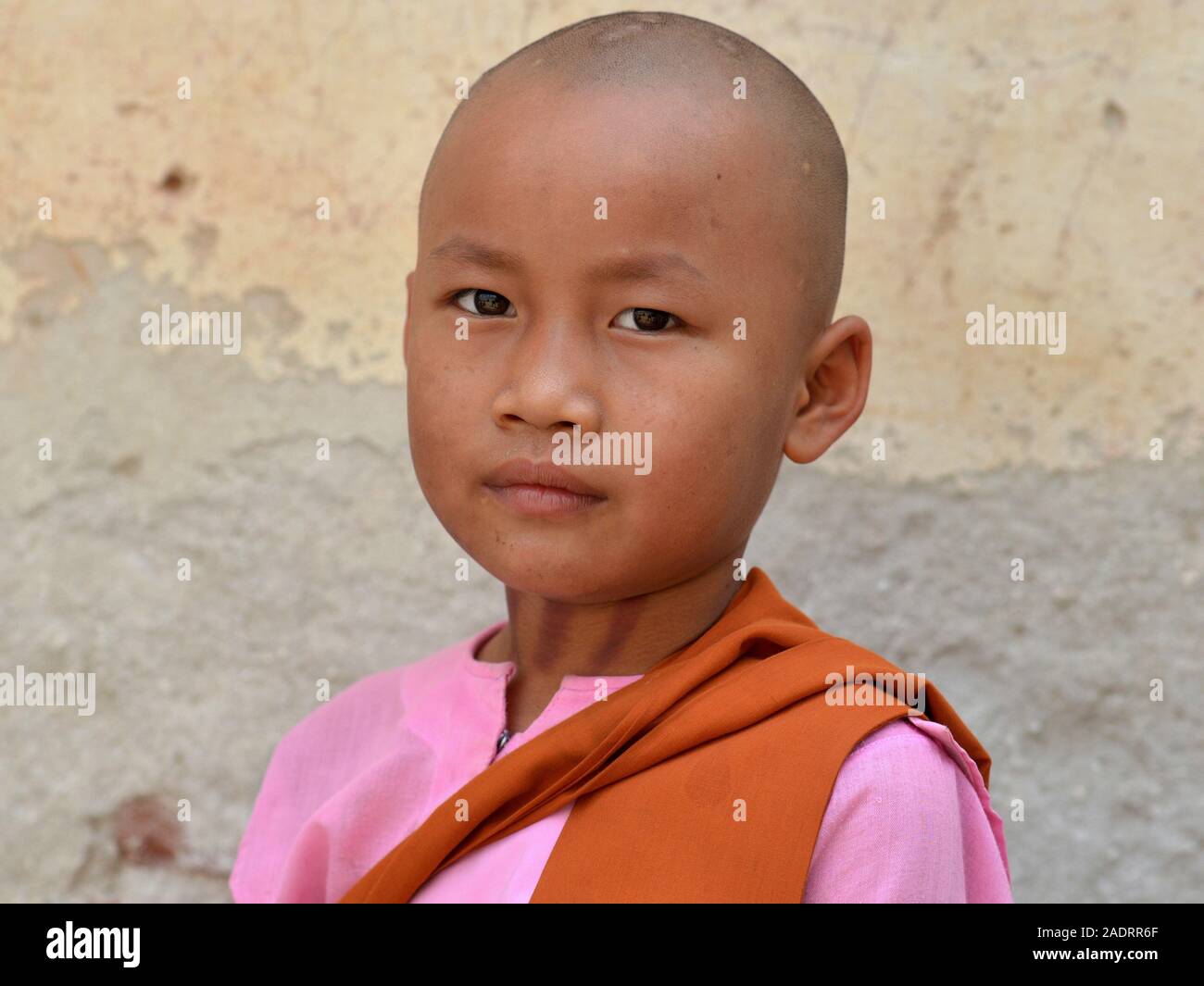 Little Burmese Buddhist girl nun (thilashin) with shaved head poses for the camera. Stock Photo