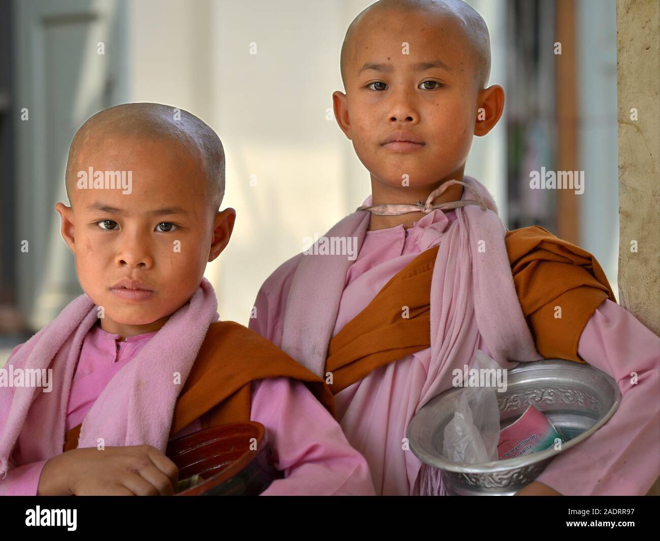 Two young Burmese Buddhist girl nuns (thilashin) carry begging bowls and pose for the camera. Stock Photo