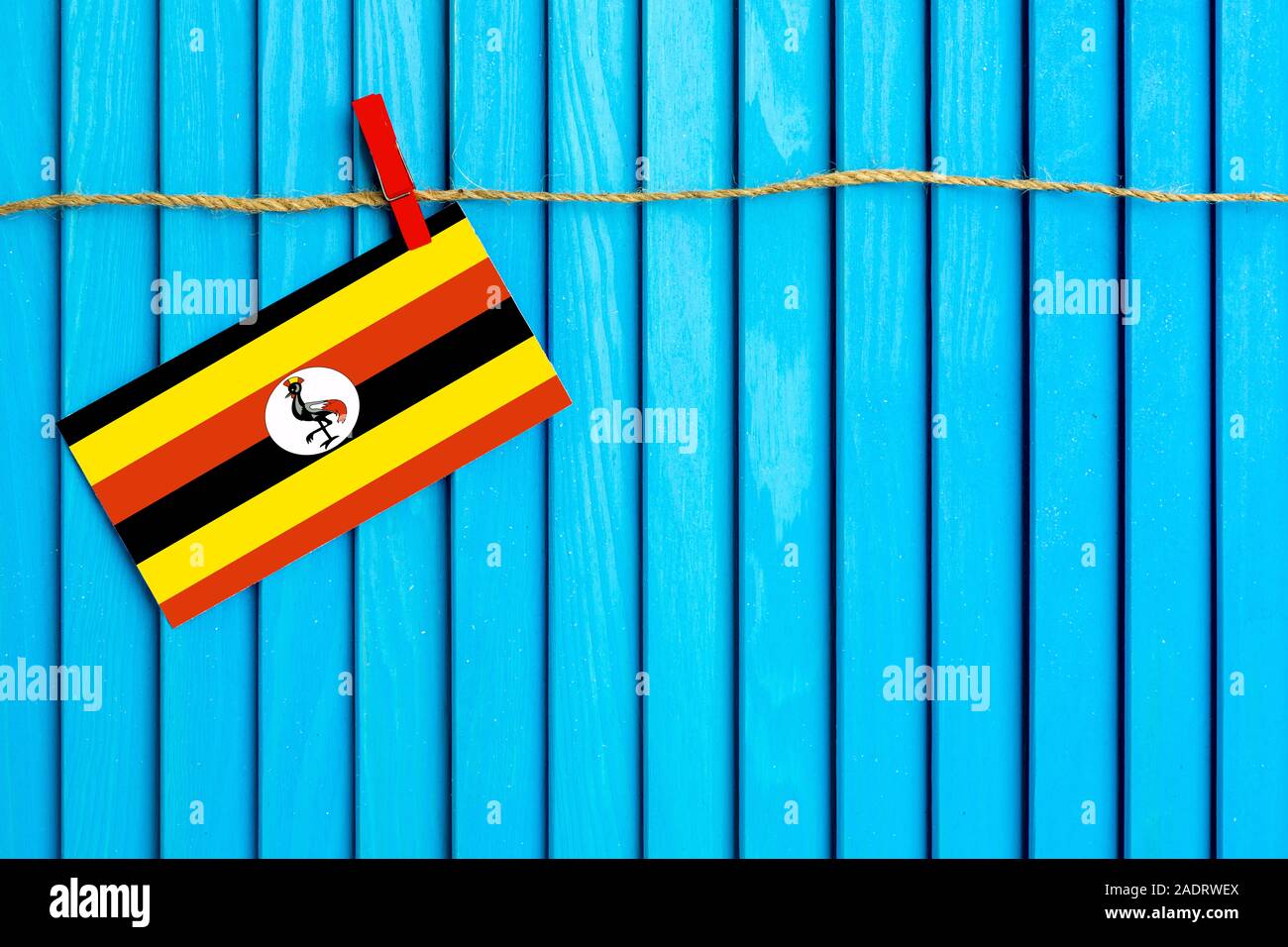 Flag of Uganda hanging on clothesline attached with wooden clothespins on aqua blue wooden background. National day concept. Stock Photo
