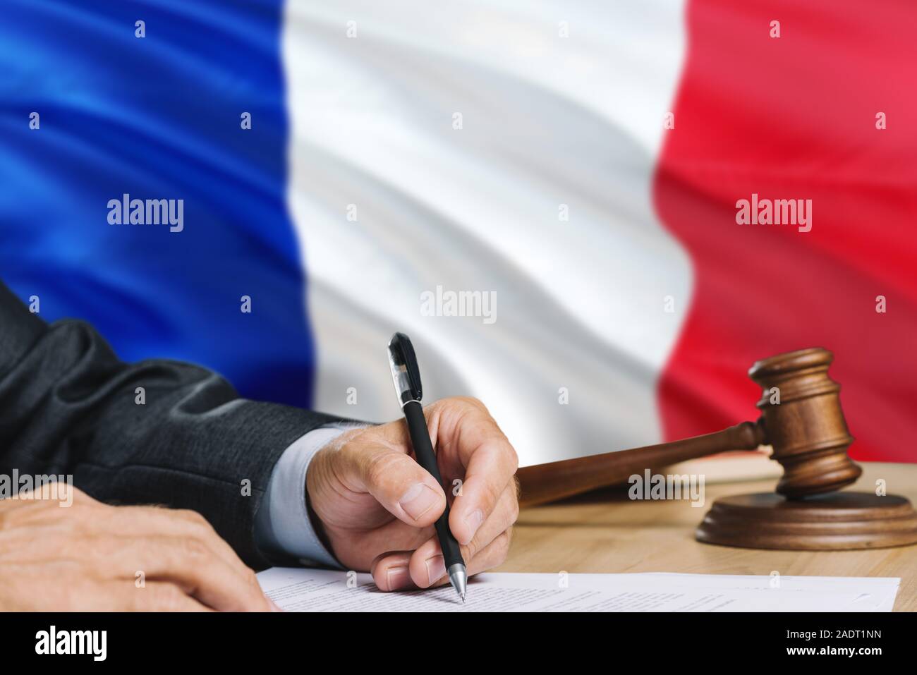 Judge writing on paper in courtroom with France flag background. Wooden