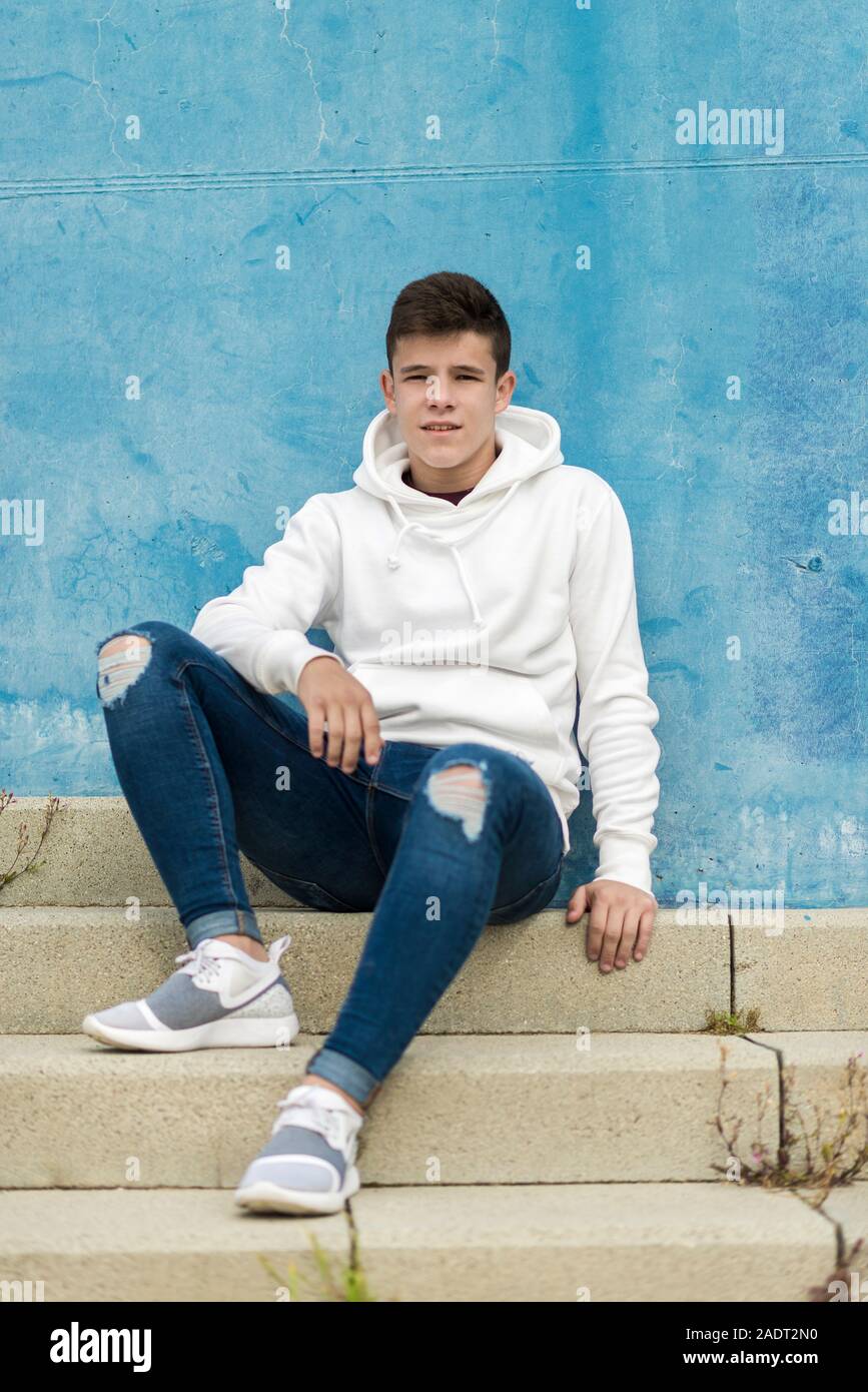 Front view of young man sitting on outdoors staircase, looking away ...