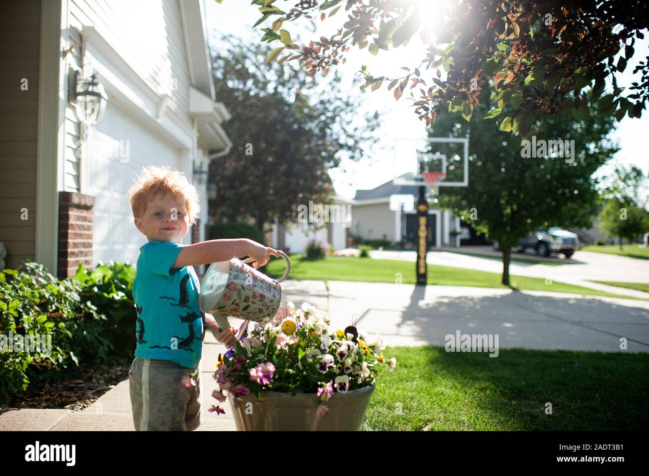 Toddler boy smiling as he waters a pot of flowers in the front yard Stock Photo