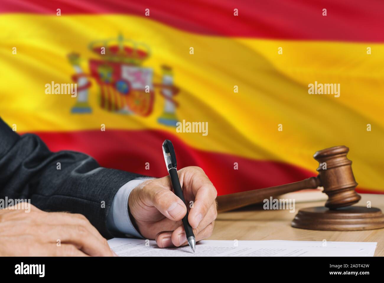 Judge writing on paper in courtroom with Spain flag background. Wooden