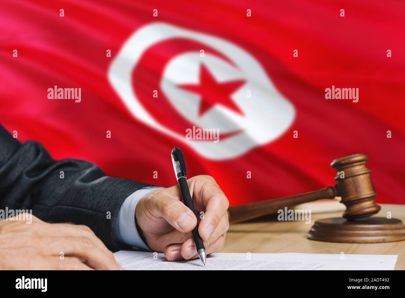 Judge Writing On Paper In Courtroom With Tunisia Flag Background 