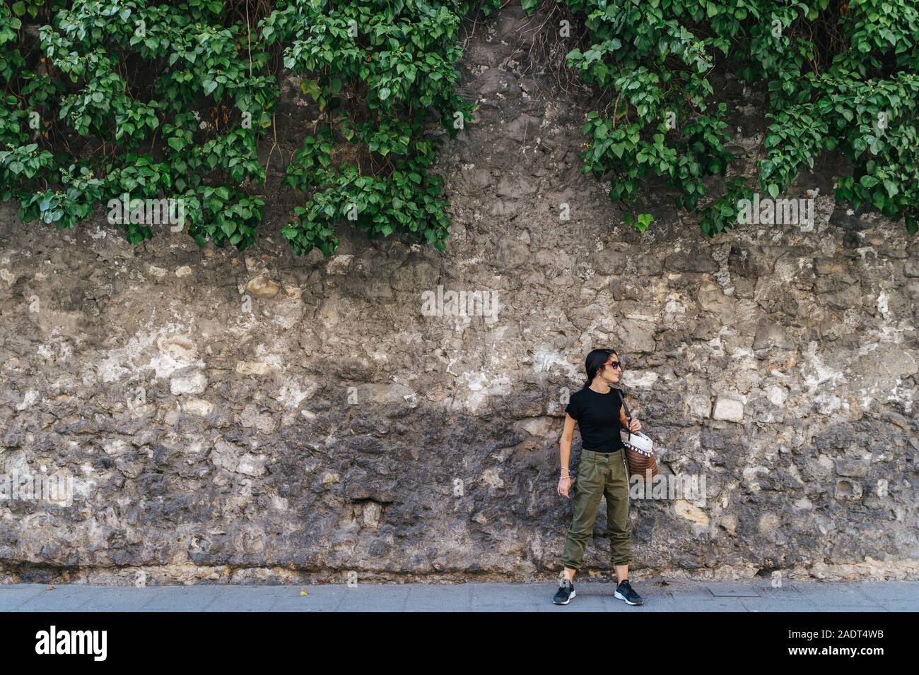 Active young woman with her bag hanging, next to a stone wall looking Stock Photo