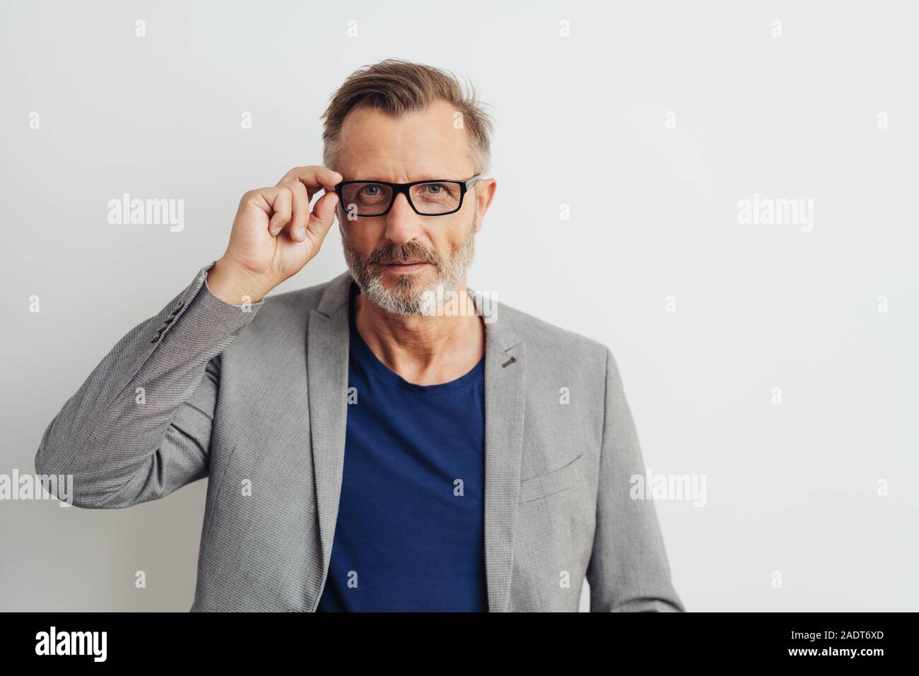 Man wearing glasses staring intently at the camera with his hand raised to  the frame and a serious expression over a white studio background with copy  Stock Photo - Alamy