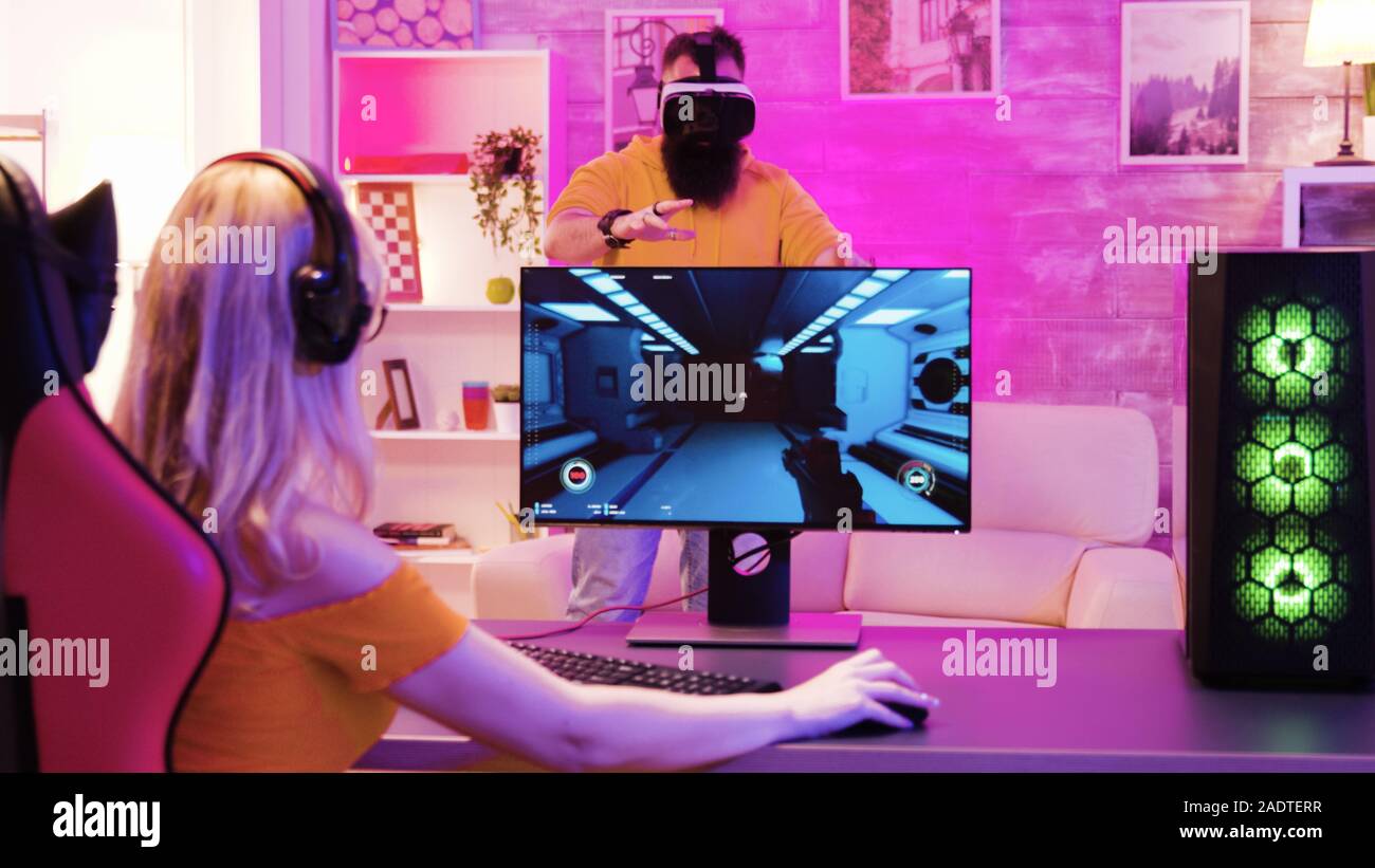 Blonde girl playing online shooter games sitting on gaming chair. Boyfriend  wearing virtual reality goggles Stock Photo - Alamy