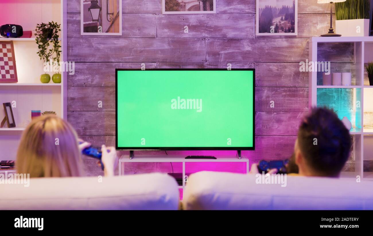 young-couple-sitting-on-sofa-and-playing-online-games-on-tv-with-green