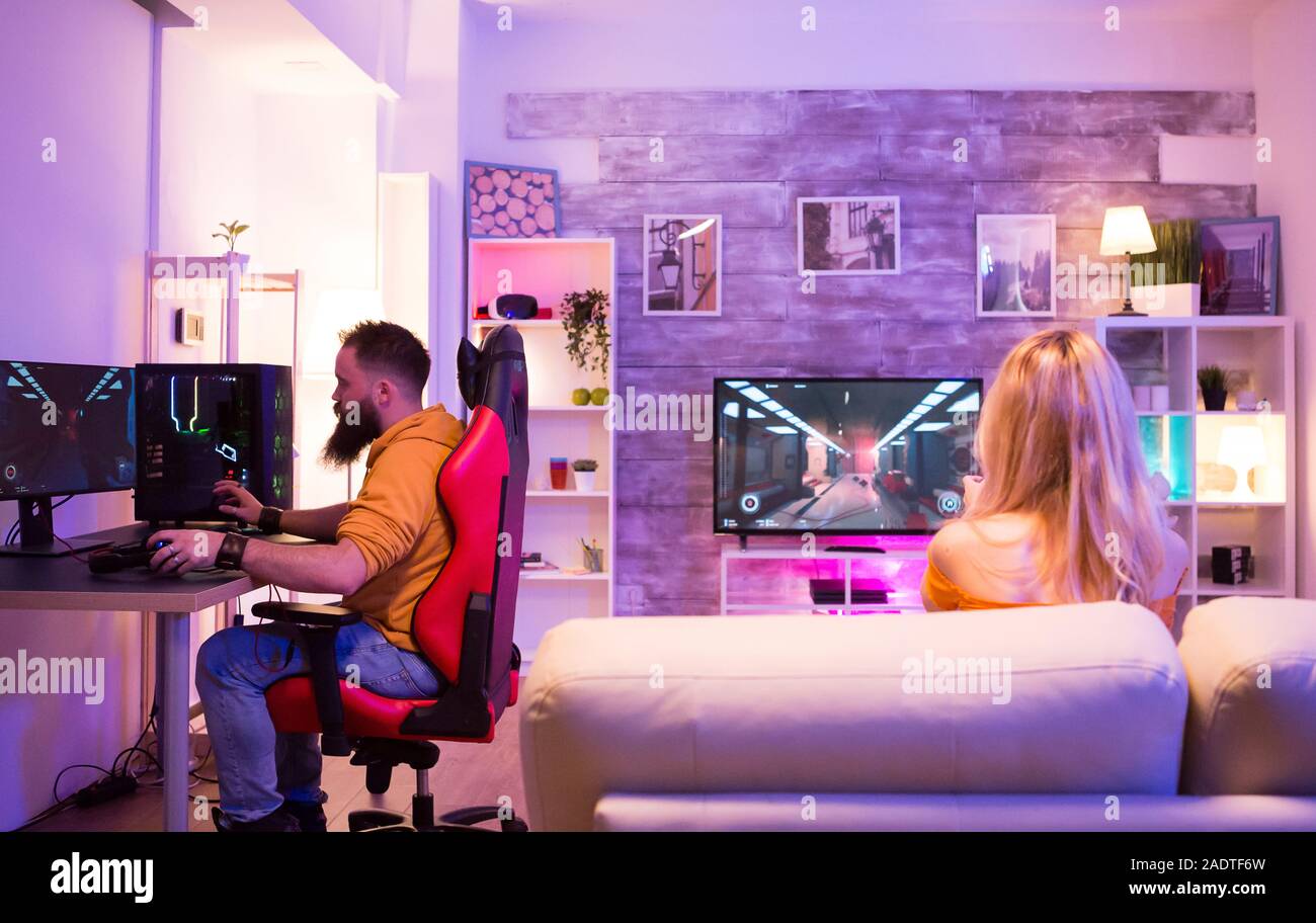Man playing shooter games and sitting on gaming chair. Girl sitting on sofa  and playing games Stock Photo - Alamy