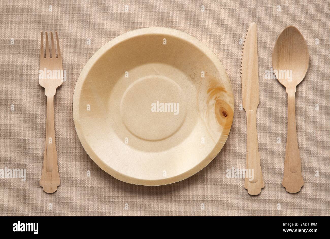 Wooden cutlery and matching empty clean plate viewed in a flat lay from above in a table setting on a woven beige linen fabric Stock Photo