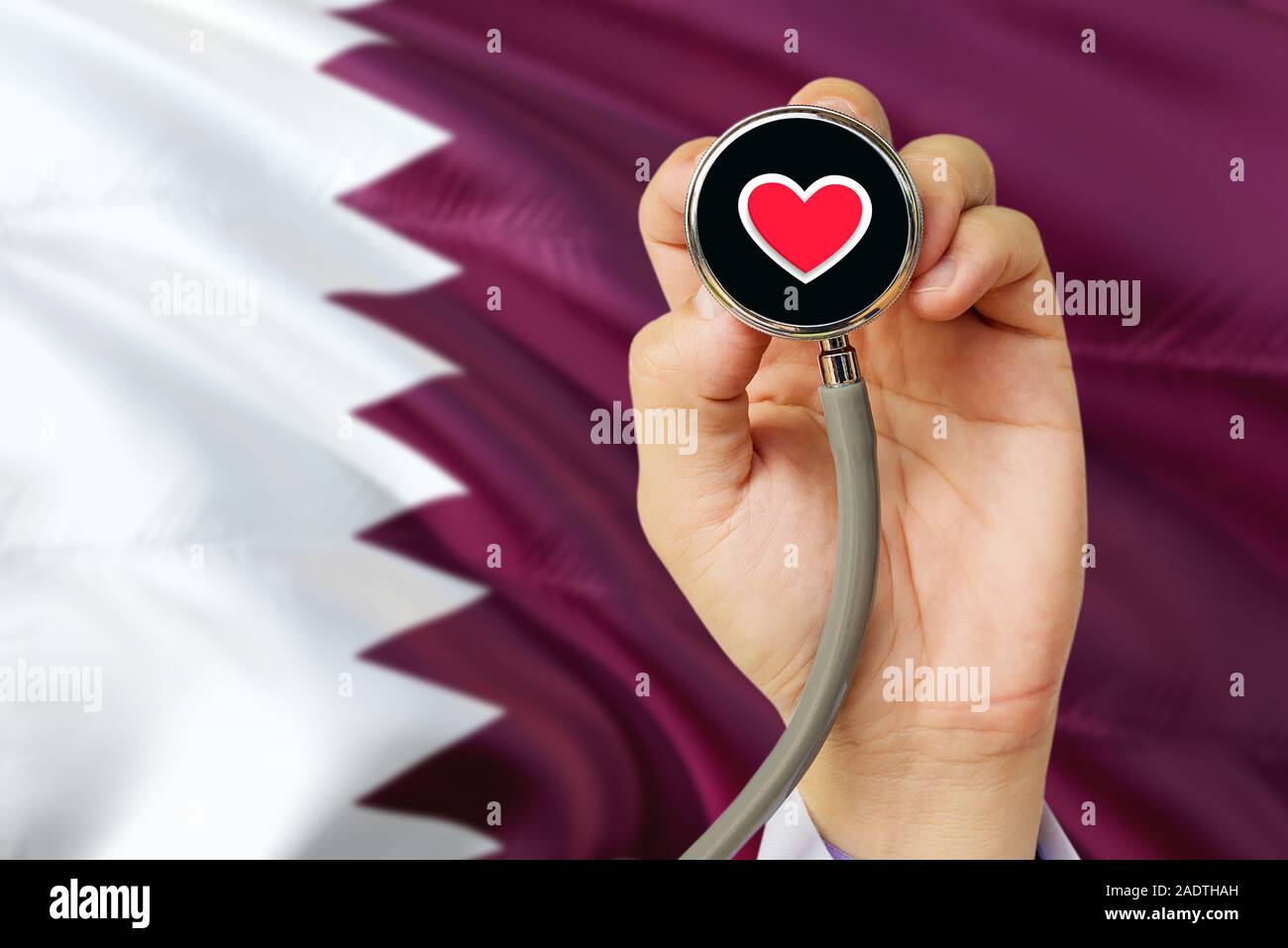Doctor holding stethoscope with red love heart. National Qatar flag