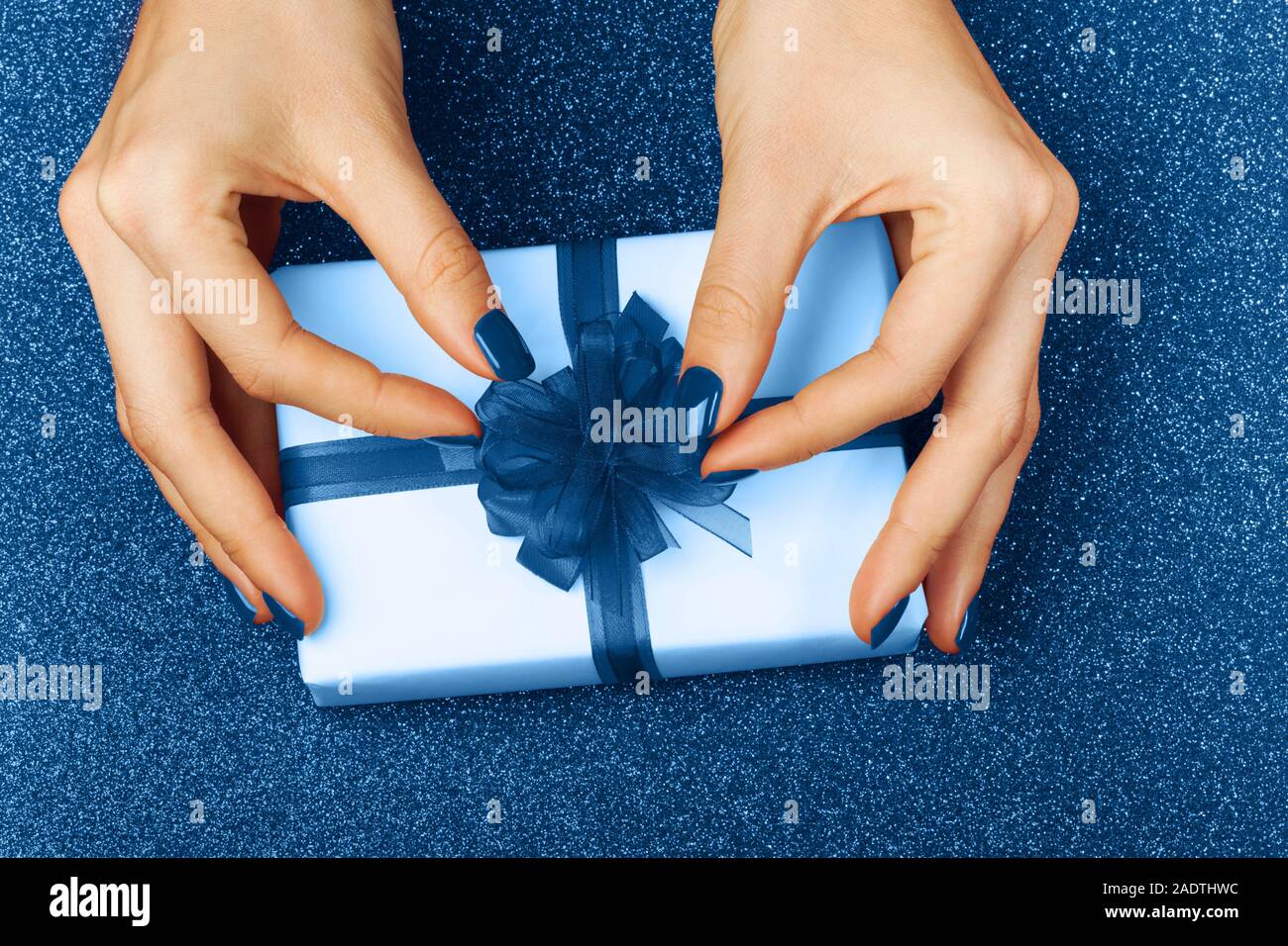 Beautiful female hands with a wrapped present on a brilliant festive blue background. Perfect manicure. Concept of the New Year, Christmas, Valentine's Day, gifts Stock Photo