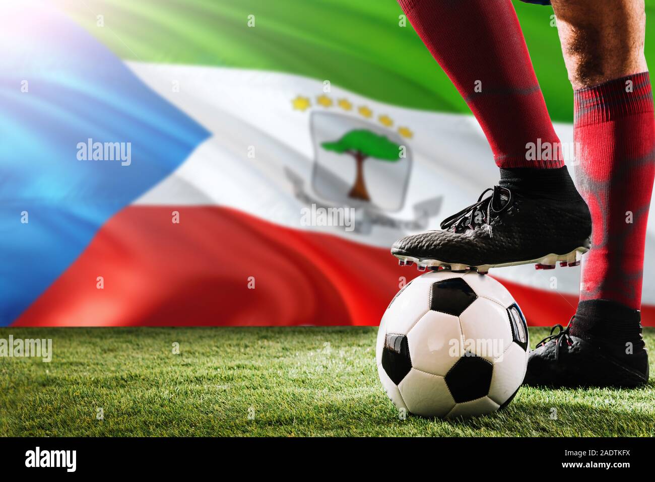 Close up legs of Equatorial Guinea football team player in red socks, shoes on soccer ball at the free kick or penalty spot playing on grass. Stock Photo