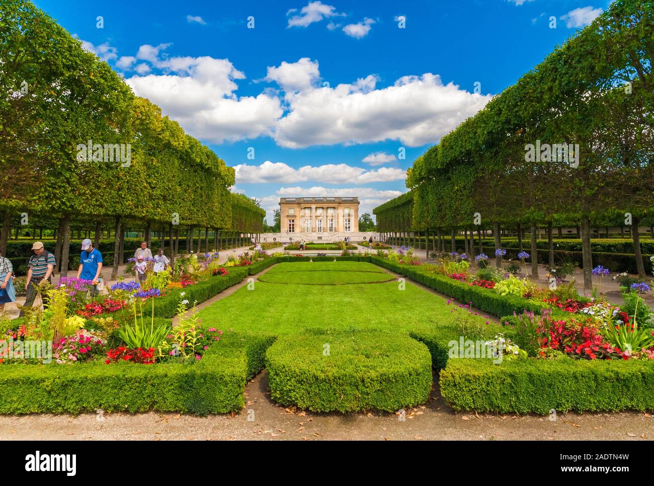 Great panoramic view of the Petit Trianon Palace in Versailles with the beautiful geometric formed garden, flanked by a row of trees on a nice summer... Stock Photo