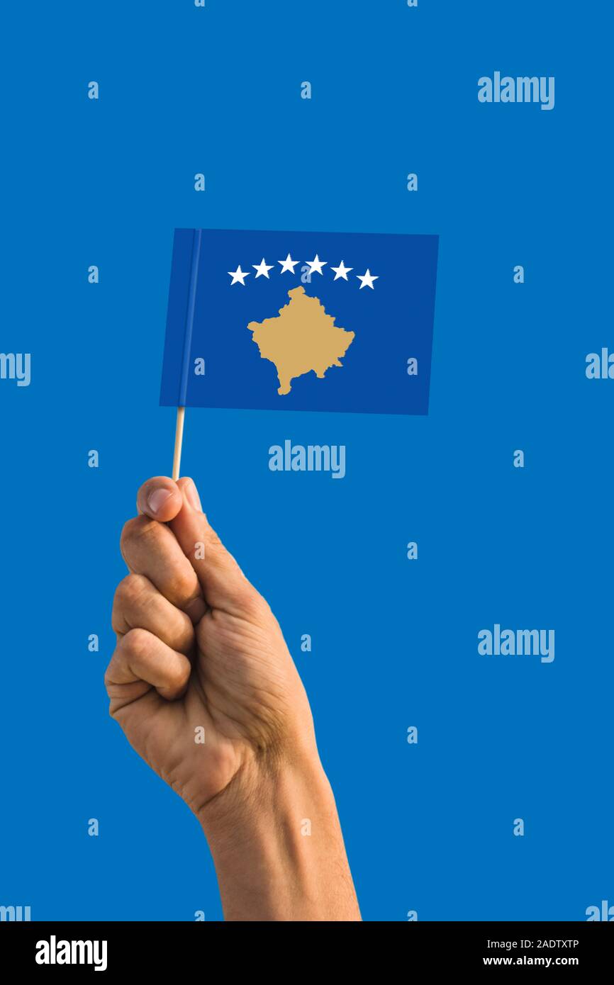 Woman hand holding Kosovo flag with stick, waving flag on deep blue sky. National theme, deep blue sky. Stock Photo
